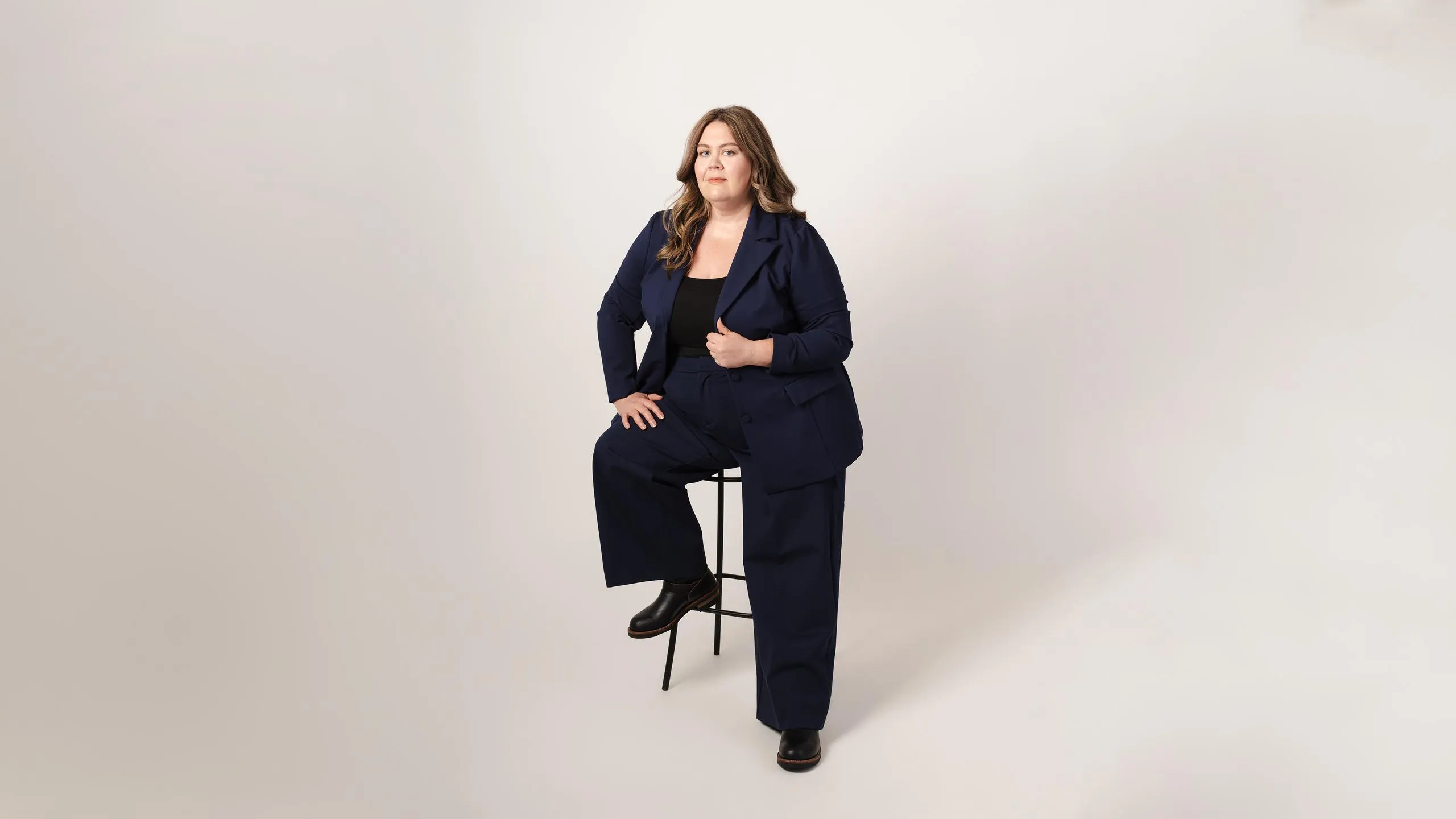 Kyle Cadotte seated on a tall stool in a navy suit and black top.